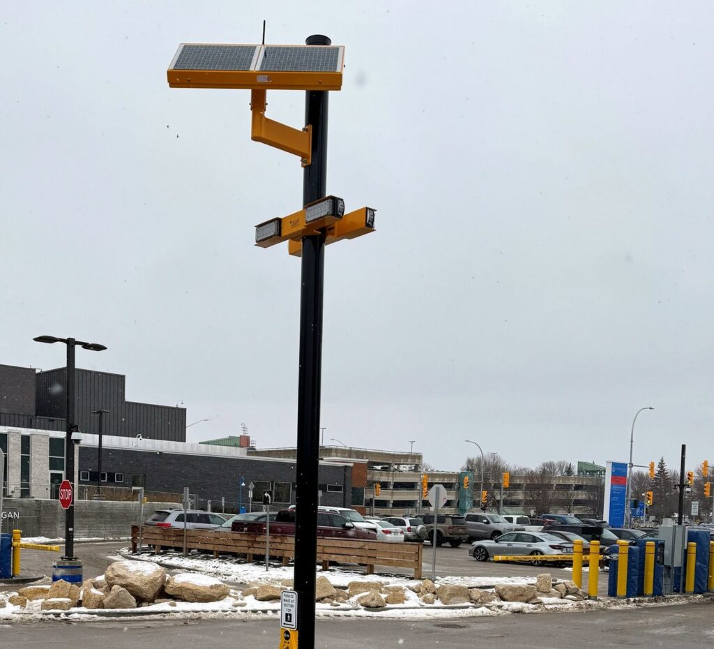 Solar-powered crosswalk beacon on a pole beside a parking lot