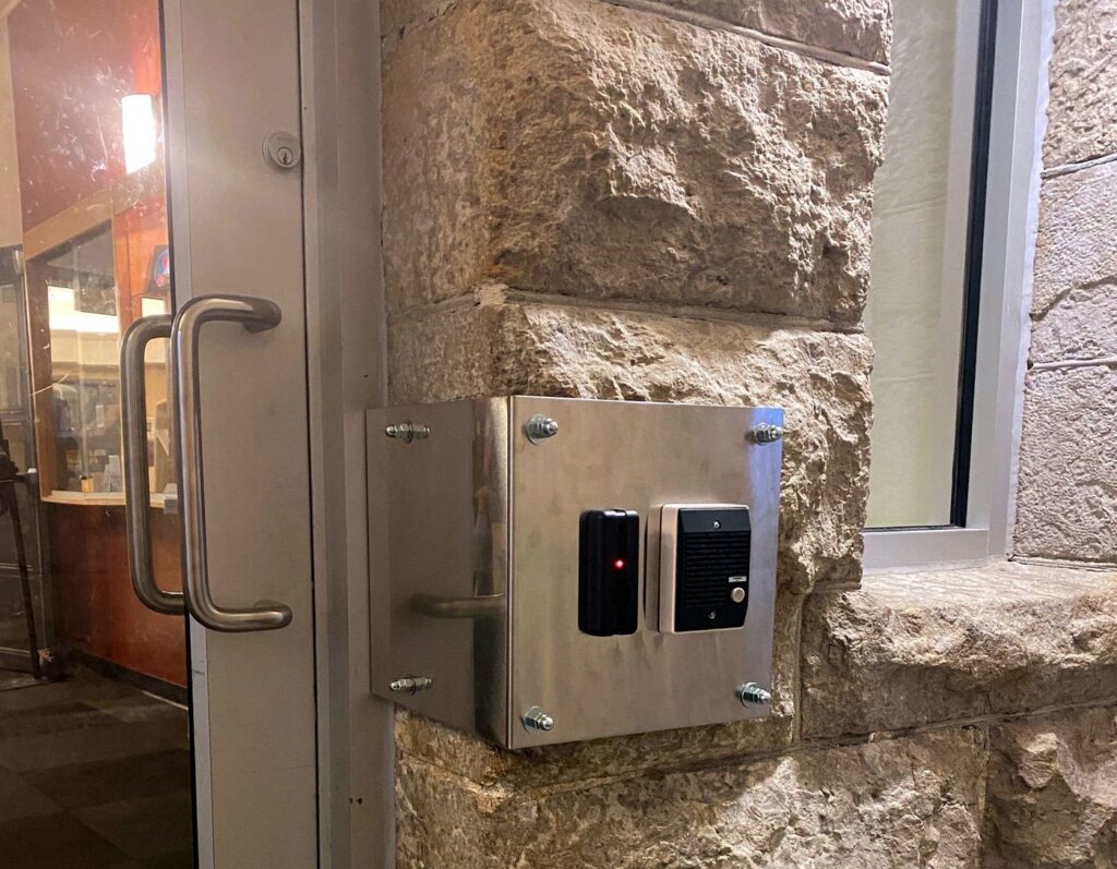 Card reader and intercom in a stainless steel enclosure mounted beside a door on a stone wall
