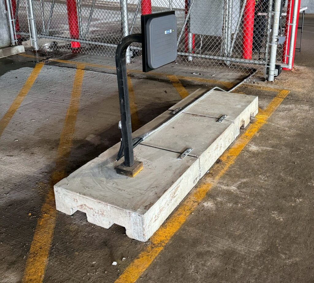 Card reader on a gooseneck post beside a sliding gate in a parkade